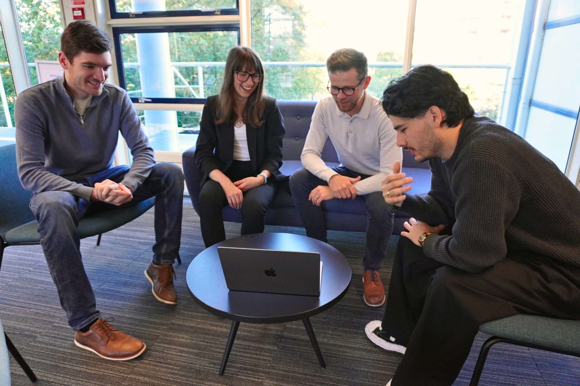 Four of the team laughing over a laptop on the sofas by the office windows