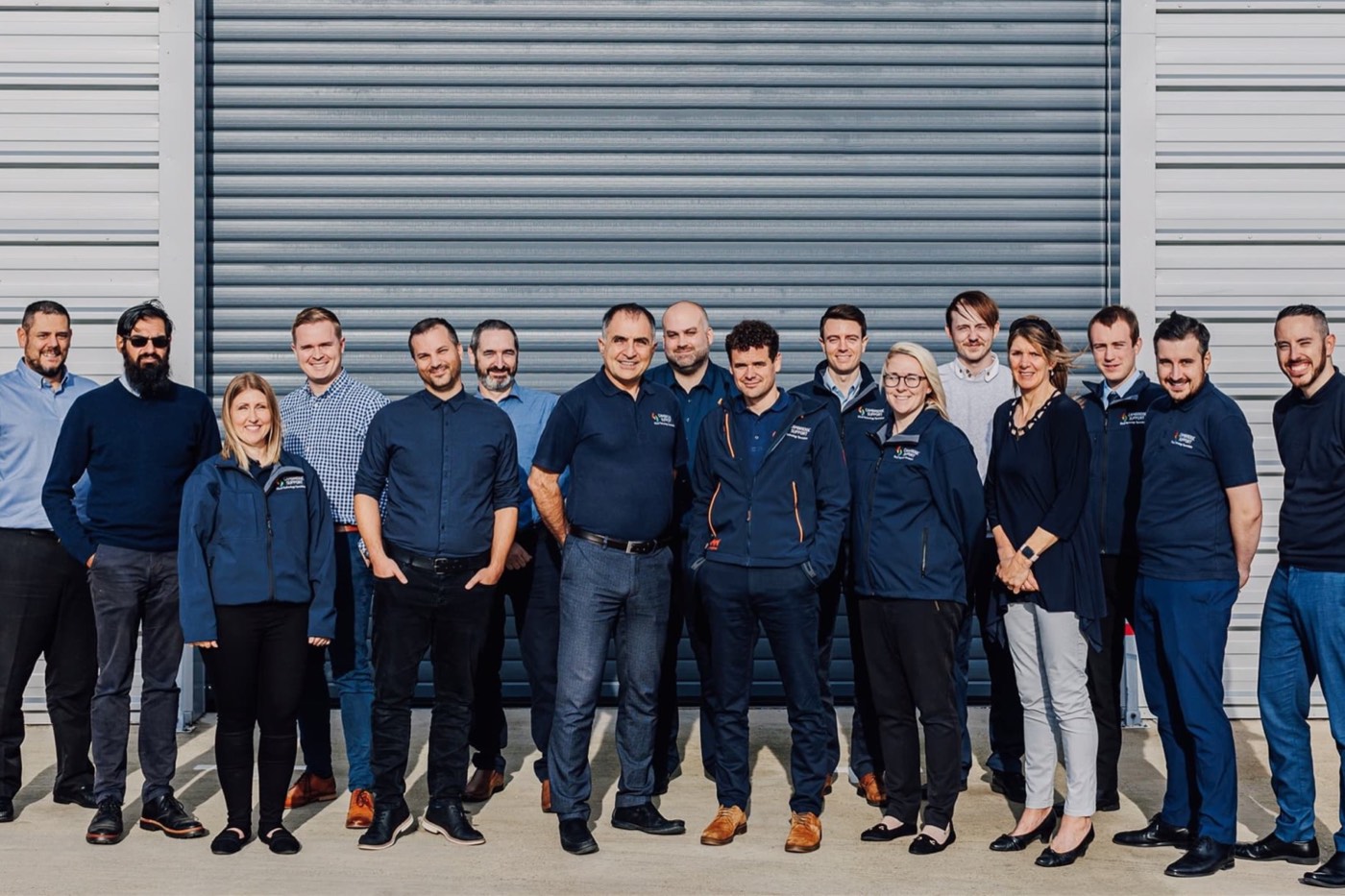 The Cambridge Support team, around twenty people in navy, standing in a row in front of a roller door.
