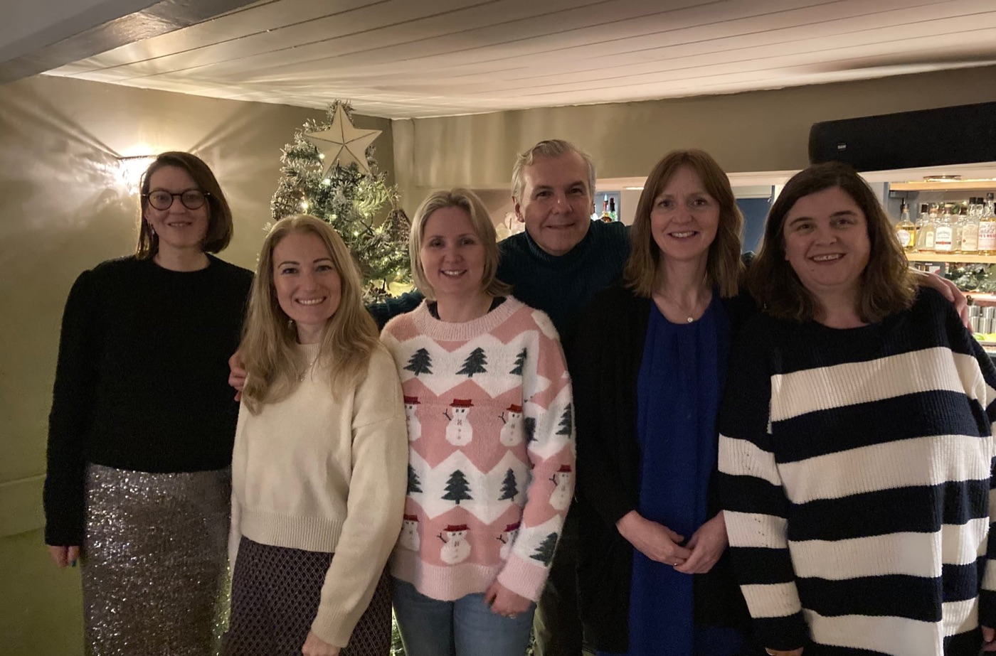 Six members of the Home-Start Cambridgeshire team smiling together beside a Christmas tree.