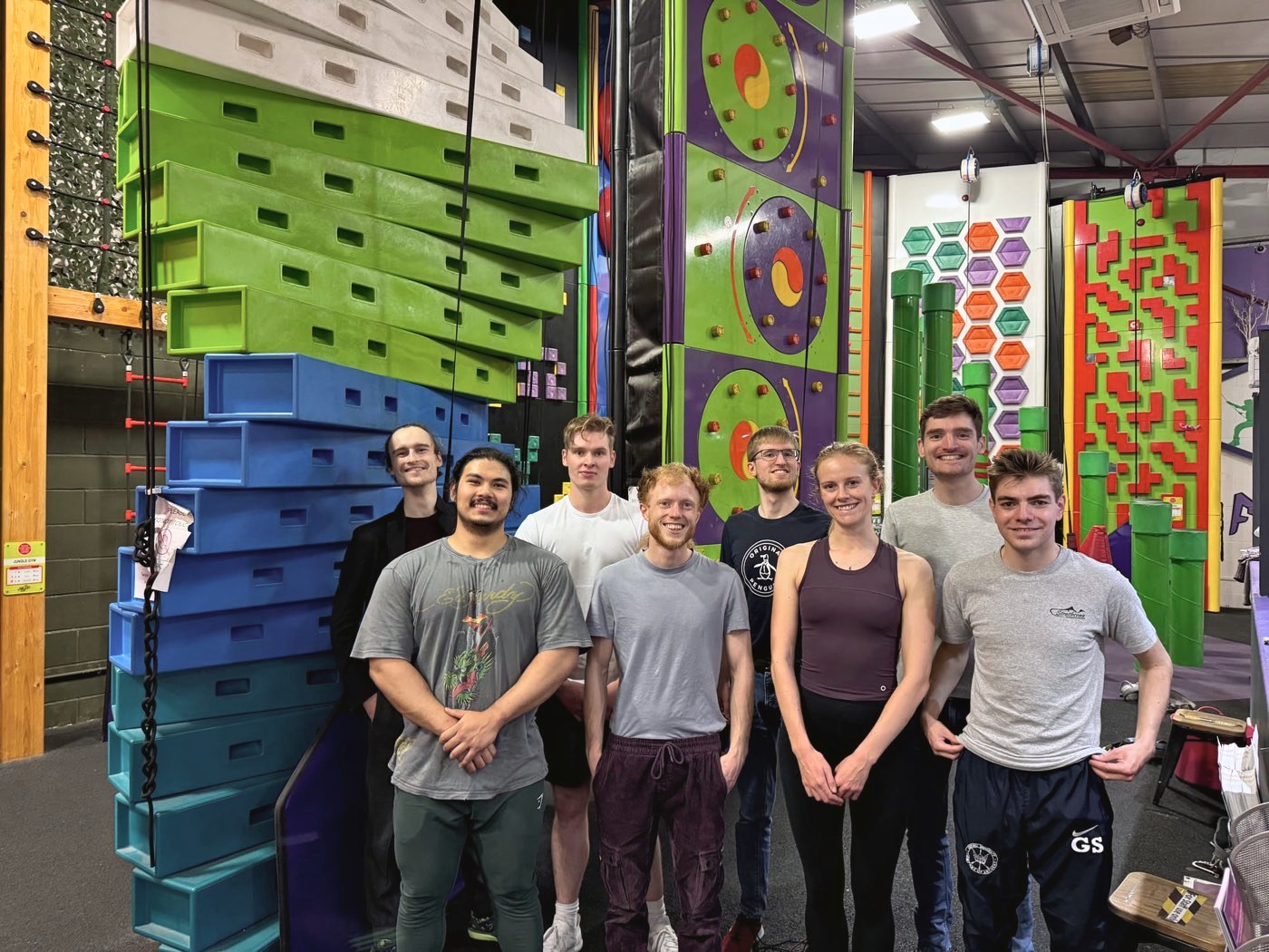 Nine members of the team smiling in front of the colourful walls at a climbing centre