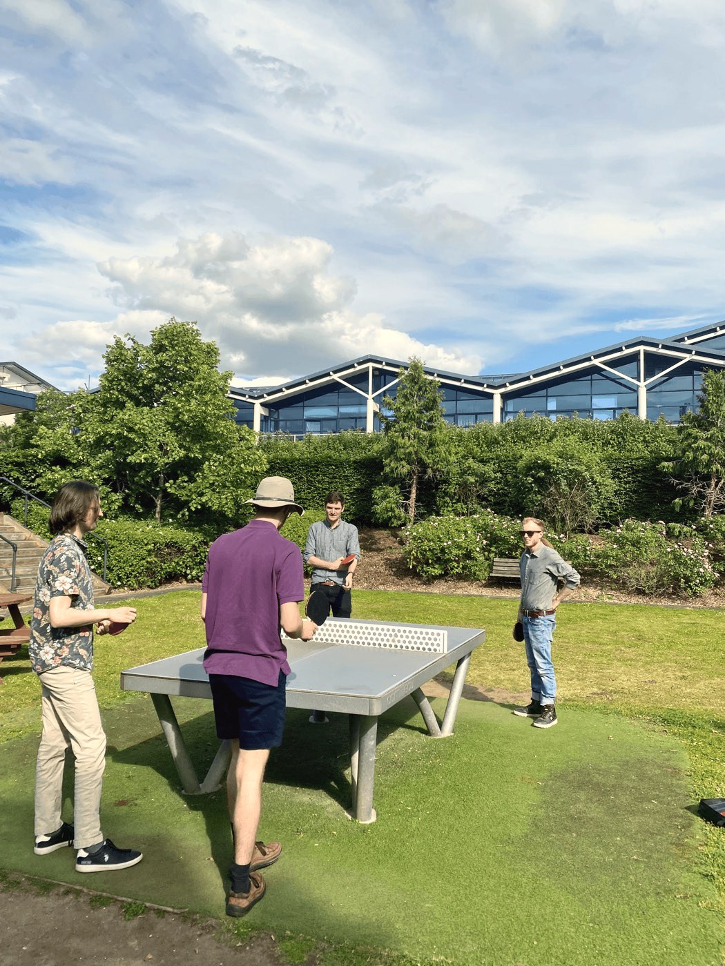 Four colleagues playing table tennis on the lawn outside the office