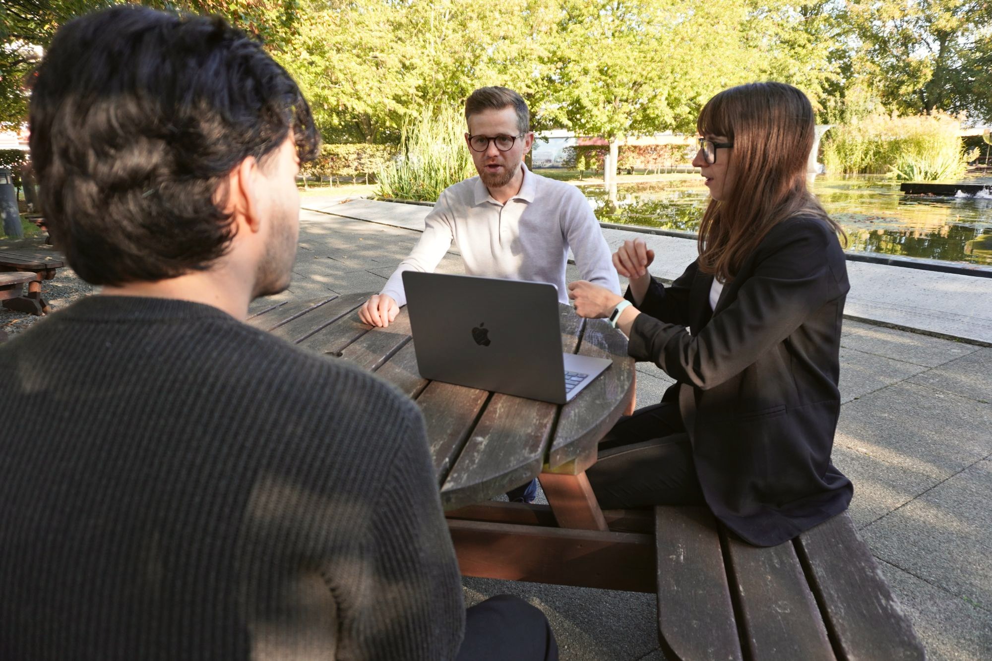 Two of our team talking a client through a project at a picnic table by a pond